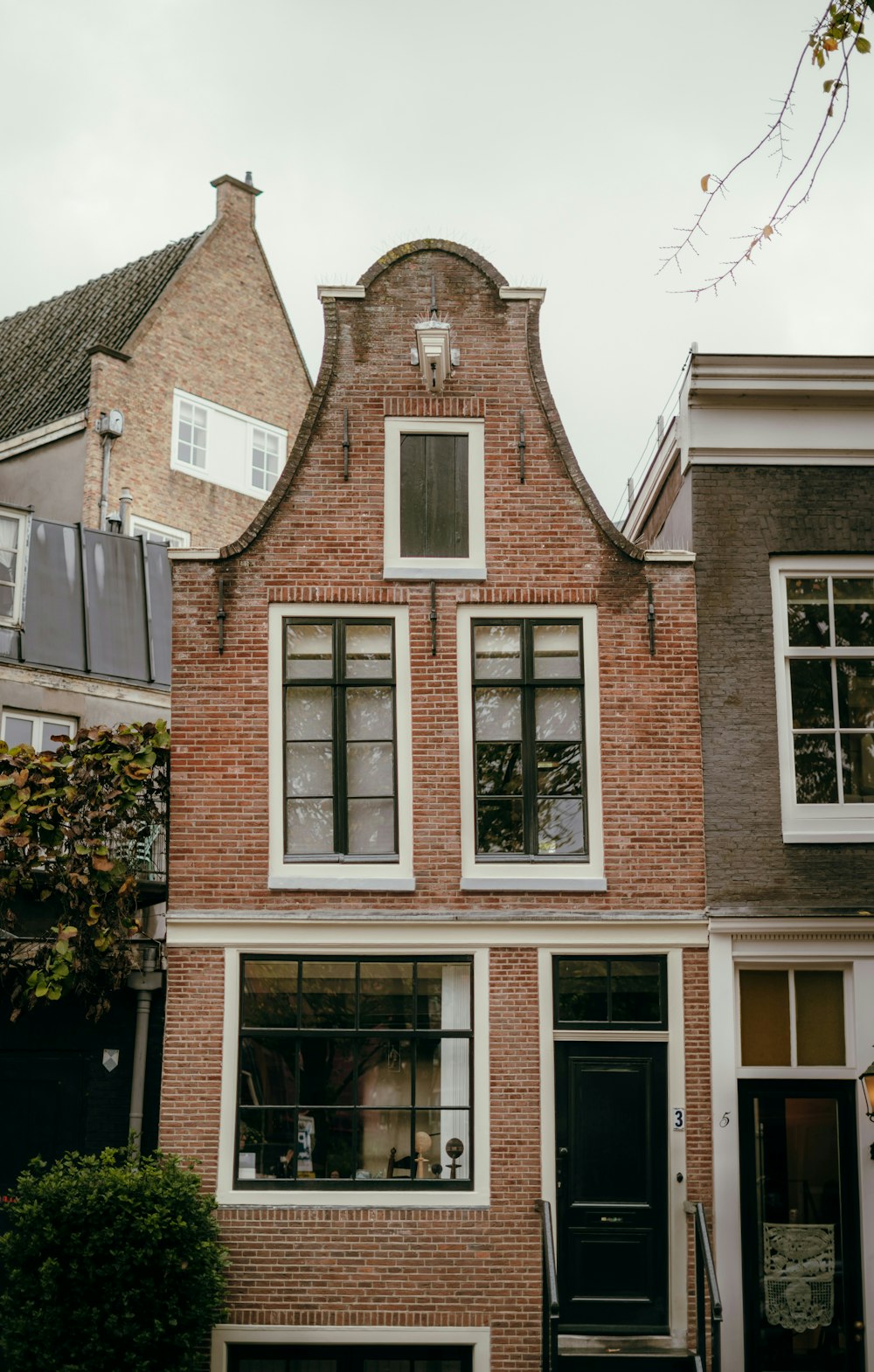 Nederlandse grachtenpandgevel met halsgevel, twee schuiframen, een zwarte voordeur en een pannendak op het buurpand
